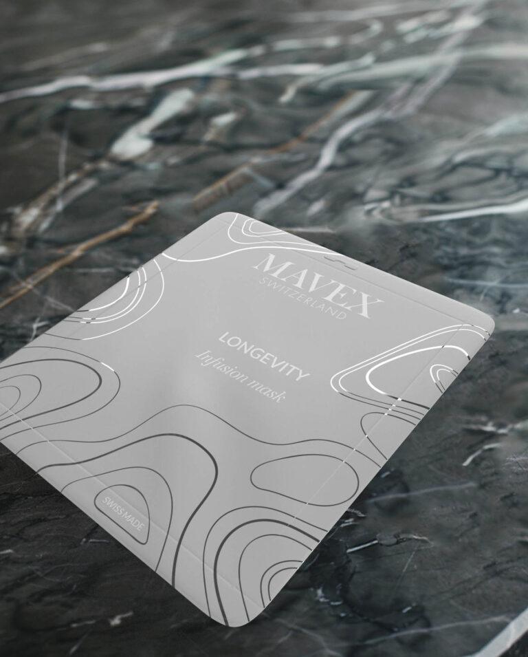 Close-up of a MAXFLEX Longevity infusion mask packaging on a dark marble surface, showing white abstract lines and 'SWISS MADE' label.