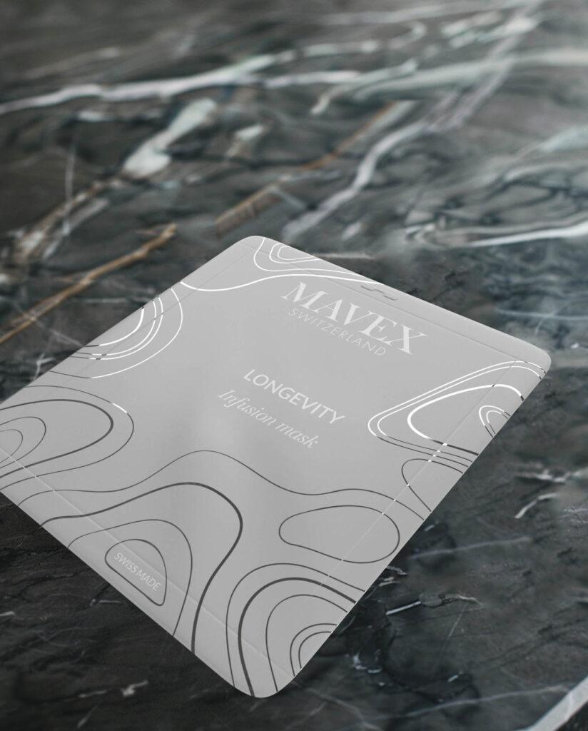 Close-up of a MAXFLEX Longevity infusion mask packaging on a dark marble surface, showing white abstract lines and 'SWISS MADE' label.