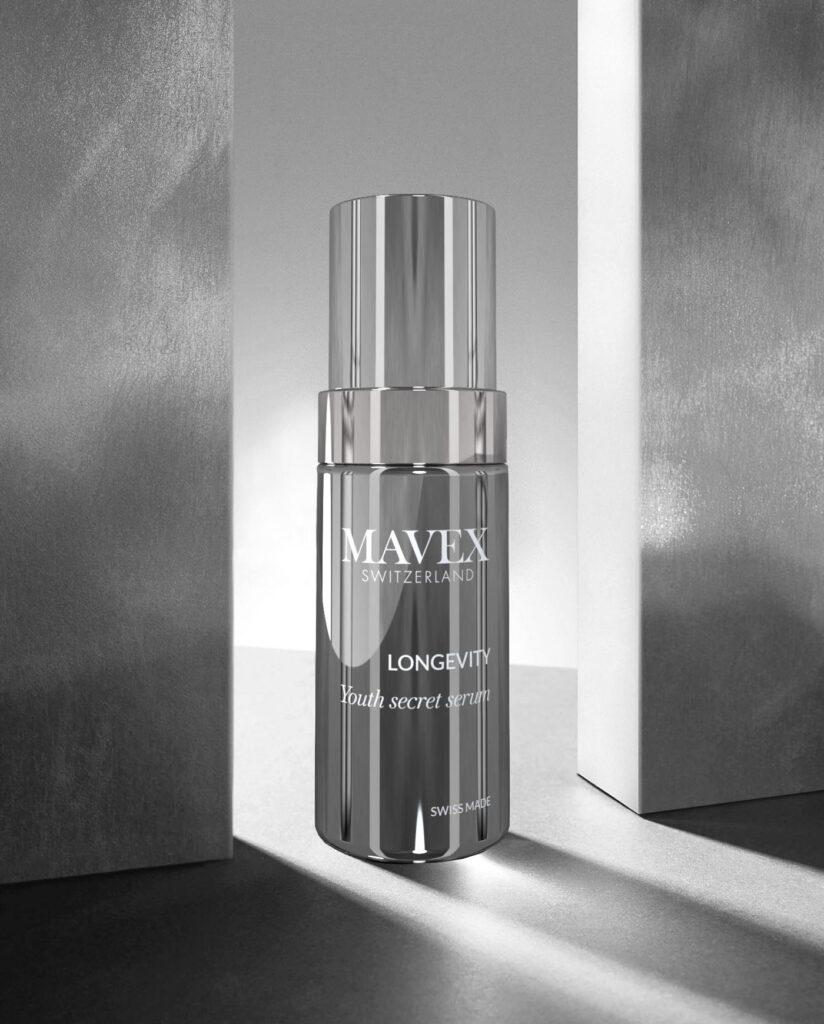 Shiny silver perfume-like bottle labeled 'MAVEX SWITZERLAND' and 'LONGEVITY' on a reflective surface between two tall gray blocks