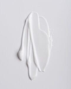 Close-up of a thick white cream smear on a white surface, showing glossy texture and smooth curves.