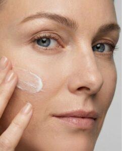 Close-up of a woman applying moisturizer to her cheek with two fingers.