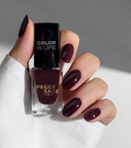 Nail polish bottle labeled Peggy Sage Paris held near burgundy-painted nails with a black cap reading Color Is Life.