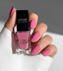 Hand with pink nails holds a pink nail polish bottle labeled Color Is Life/ Peggy Sage Paris.