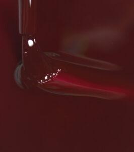 Close-up of red wine swirling inside a glass as it is poured or stirred, creating ripples and highlights in a dark background.