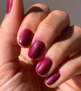 Close-up of a hand showing burgundy-purple glittery manicured nails on short to medium length nails