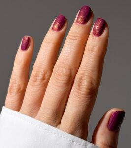 Close-up of a hand with glittery purple nail polish on the fingernails, wearing a white cuffed sleeve