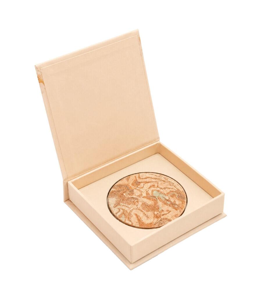 Round marble-patterned compact powder in a beige case inside an open cream-colored box (cosmetics product)