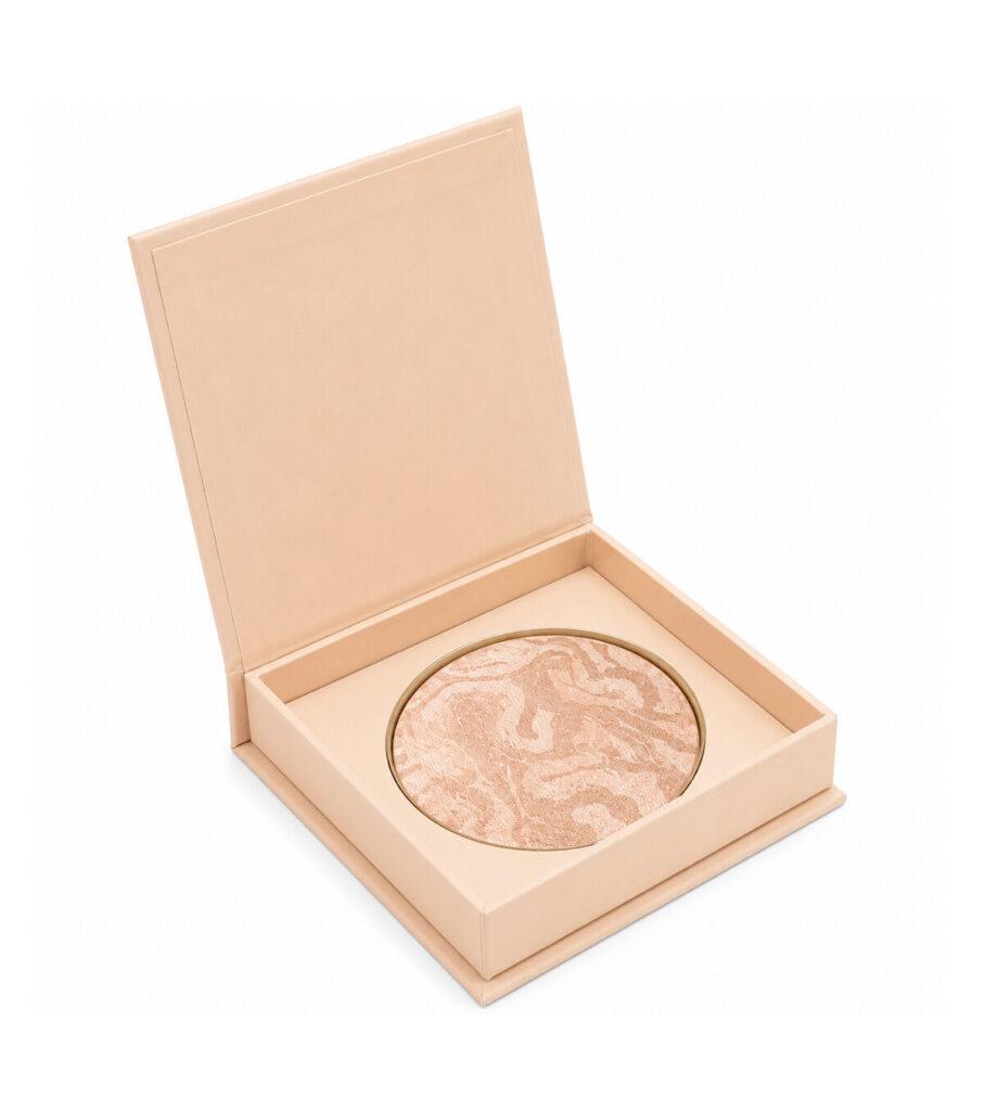 Round pressed powder/highlighter with a beige marble pattern in an open pale-pink/beige box.