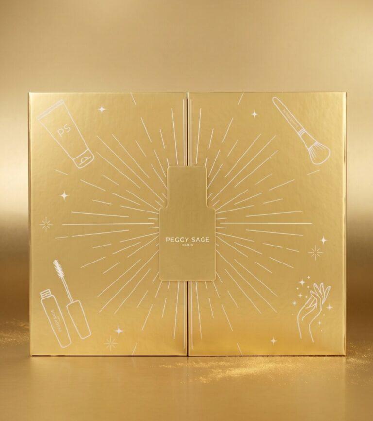 Gold-toned makeup gift box with a central rectangular bottle design and sunburst lines, Peggy Sage Paris text in the center.